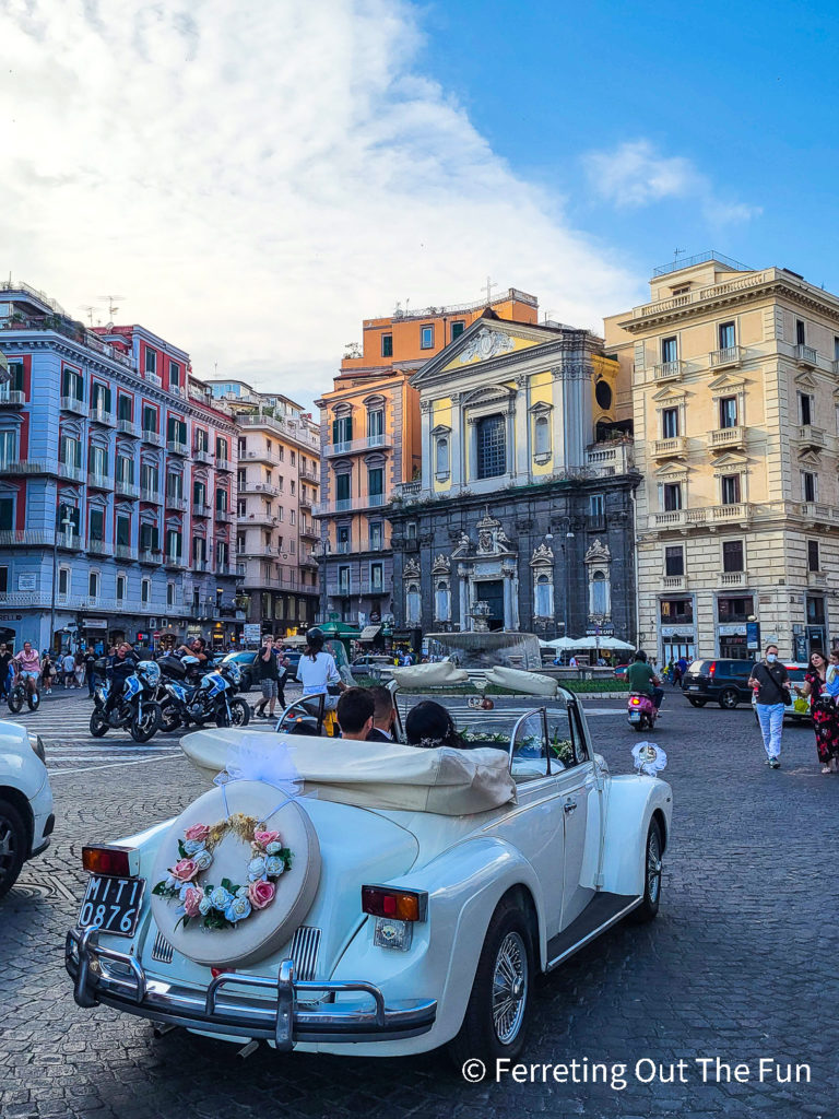 Newlyweds in a vintage white convertible in the historic center of Naples, Italy