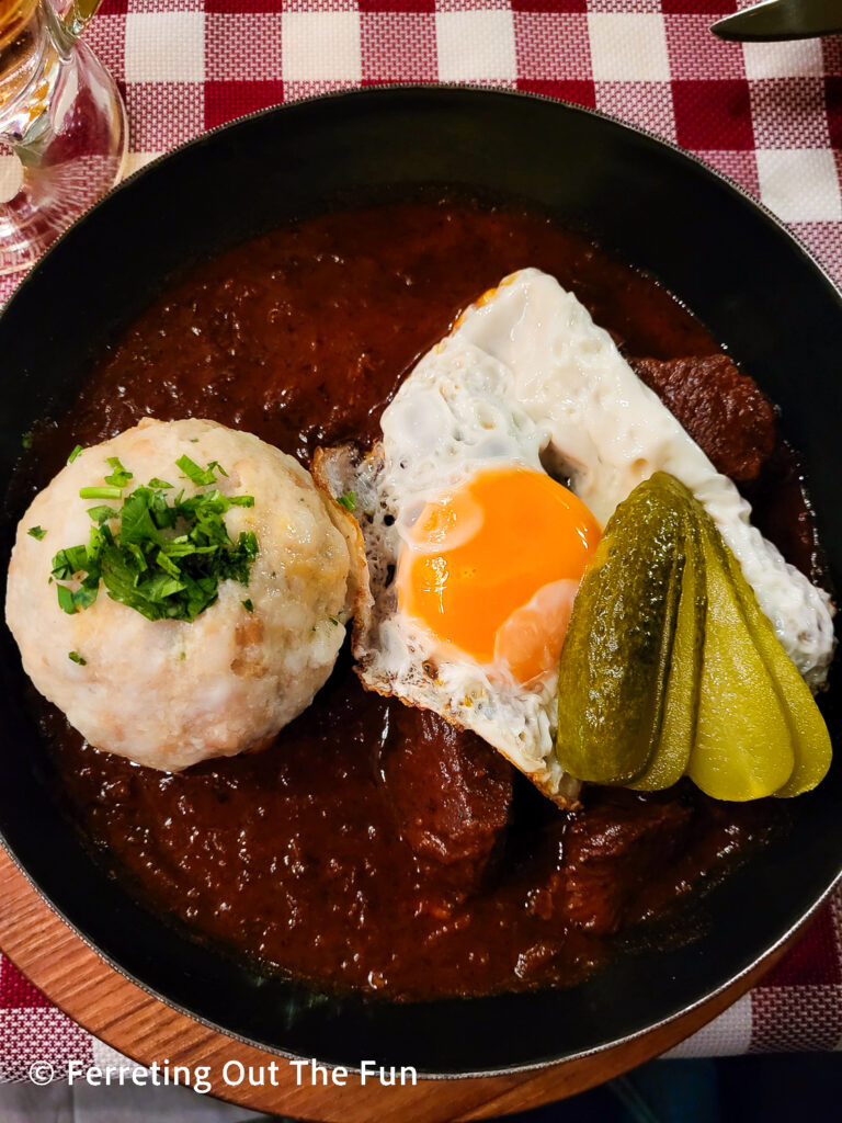 Beef goulash with pickles, a dumpling, and fried egg at Wiener Wiaz Haus restaurant in Vienna