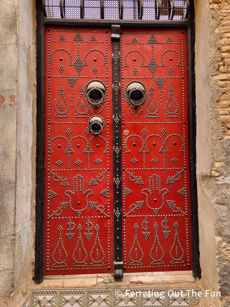 A beautiful red door with three knockers and elaborate nail head designs in Tozeur, Tunisia